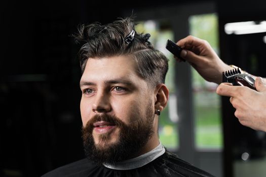 Barber making hairstyle for confident bearded hipster. Advertising for barbershop and men's beauty salon