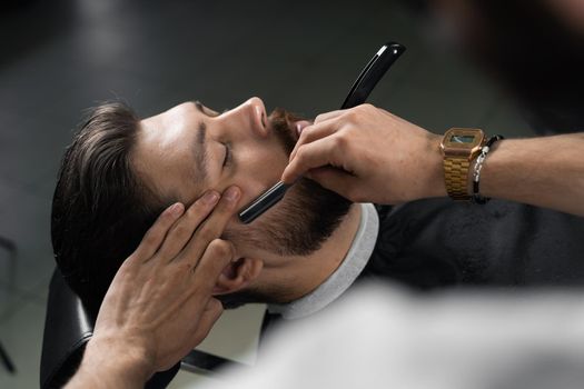 Straight razor cut mans beard in barbershop. Barber man making hairstyle for handsome man