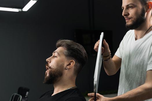 Happy and surprised bearded man looking in mirror in barbershop. Showing result of low fade machine hair.