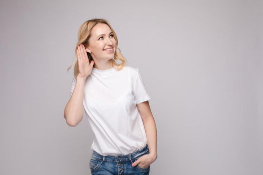 Studio portrait of curious brunette girl in multicolored top listening to the news or gossips with her ear.