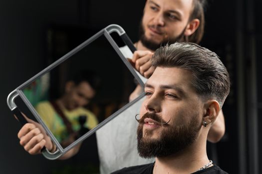 Barber with dreadlocks showing result of low fade machine hair and beard cut for bearded man in barbershop. Hairstyle with a smooth transition