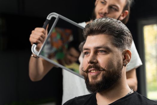 Barber with dreadlocks showing result of low fade machine hair and beard cut for bearded man in barbershop. Hairstyle with a smooth transition