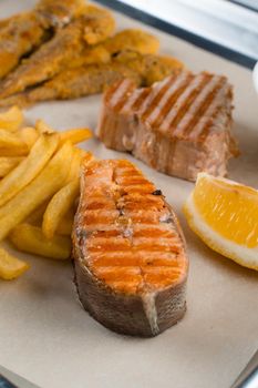 Grilled salmon steak with lemon and fries on light background