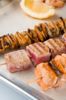 Barbecue seafood kebab with grilled mussels, tuna, salmon on a wooden skewer with white sauce and lemon