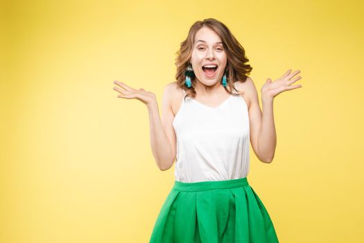 Studio portrait of attractive young caucasian brunette in casual outlook covering her mouth in shock or astonishment. She is shocked, stupified or surprised. Looking at camera with shocked facial expression on yellow background.