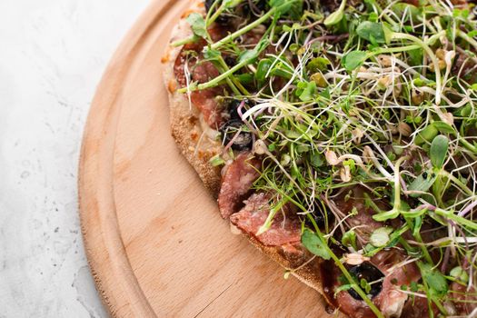 Pinsa romana with salami, cheese, mushrooms, decorated with microgreens on wooden boardon white background