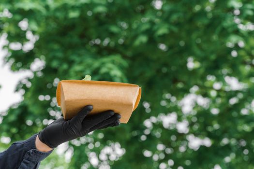 Salad in eco thermo box on a green backround in the park. Safety delivery with mask and black medical gloves at quarantine. On line order from the restaurant delivered to people who stay at home.