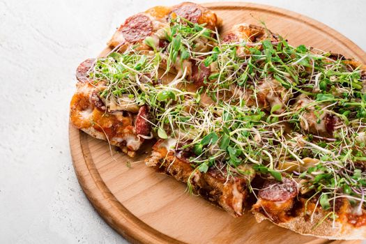 Pinsa romana with salami, cheese, mushrooms, decorated with microgreens on wooden boardon white background