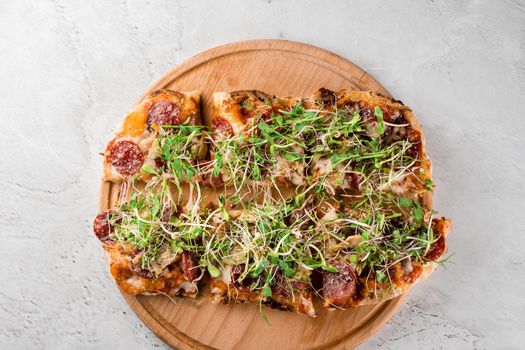 Pinsa romana with salami, cheese, mushrooms, decorated with microgreens on wooden boardon white background