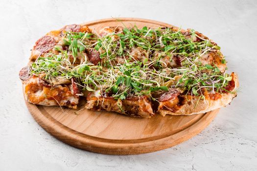 Pinsa romana with salami, cheese, mushrooms, decorated with microgreens on wooden boardon white background