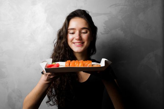 Girl holding philadelphia rolls in a paper box on gray background. Sushi, food delivery