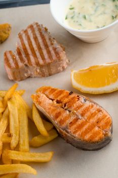 Grilled salmon steak with lemon and fries on light background