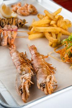 Set of seafood with large grilled shrimps on metal plate with carrot, lettuce close-up