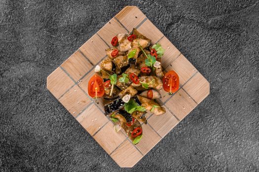 Fried eggplants on a wooden board, decorated with chili, garlic, cilantro, sesame seeds on a gray background