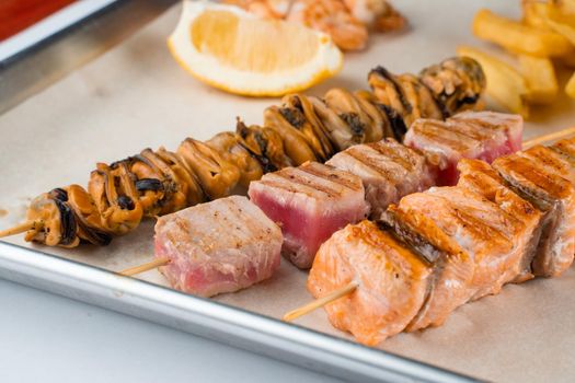 Barbecue seafood kebab with grilled mussels, tuna, salmon on a wooden skewer with white sauce and lemon
