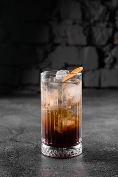 Cocktail in glass with cola, alcohol, ice, decorated dried orange on gray background
