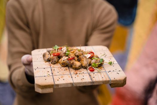 Fried mussels with chili, garlic, sesame, herbs, on square wooden board. Serving the dish by the waiter