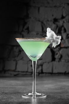 Green alcohol cocktail in a glass decorated with cotton candy on gray background