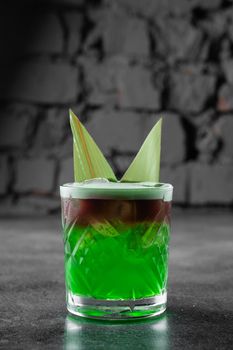 Green layered cocktail decorated with bamboo leaves on a gray background