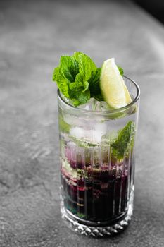 Cocktail with tonic, currant syrup, lime, mint, ice in tall glass on gray background. Puff cold drink with blueberries