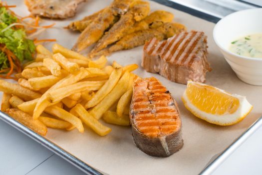 Grilled salmon steak with lemon and fries on light background