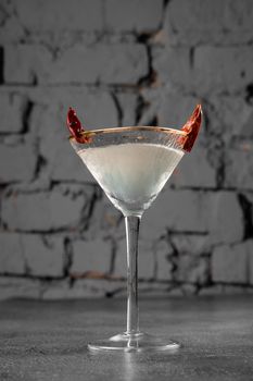 Cocktail in glass with chili on gray background. Devil alcohol drink