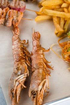 Set of seafood with large grilled shrimps on metal plate with carrot, lettuce close-up