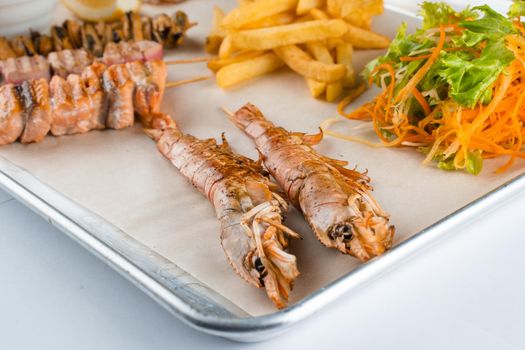 Set of seafood with large grilled shrimps on metal plate with carrot, lettuce close-up