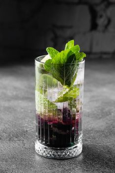 Cocktail with tonic, currant syrup, lime, mint, ice in tall glass on gray background. Puff cold drink with blueberries