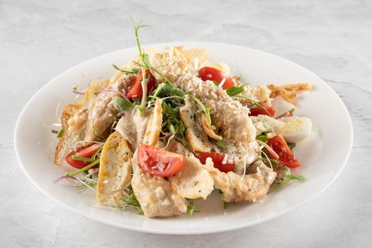 Caesar salad with chicken, parmesan, cherry tomato, lettuce, croutons, egg on white plate on light table