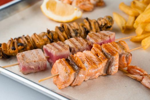 Barbecue seafood kebab with grilled mussels, tuna, salmon on a wooden skewer with white sauce and lemon