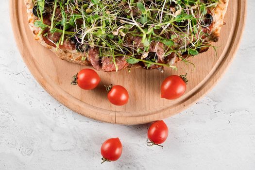 Pinsa romana with salami, cheese, mushrooms, decorated with microgreens on wooden boardon white background