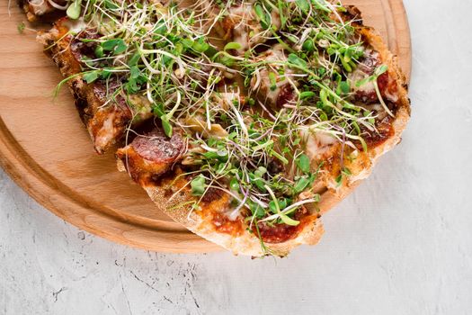 Pinsa romana with salami, cheese, mushrooms, decorated with microgreens on wooden boardon white background