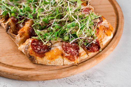 Pinsa romana with salami, cheese, mushrooms, decorated with microgreens on wooden boardon white background