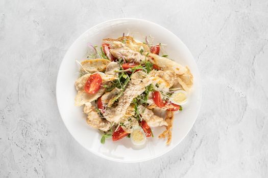 Caesar salad with chicken, parmesan, cherry tomato, lettuce, croutons, egg on white plate on light table.