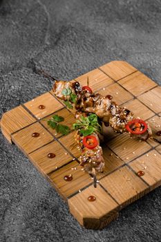 Meat on wooden skewers, garnished with cilantro, sesame, chili on square board on gray background