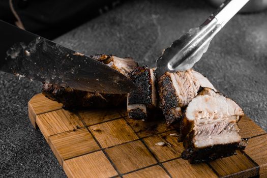 Grilled ribs slicing on a wooden plate on a gray background. Barbecue decoration