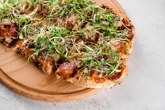 Pinsa romana with salami, cheese, mushrooms, decorated with microgreens on wooden boardon white background