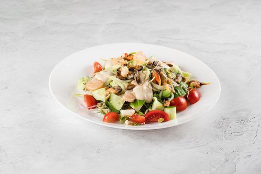 Salad with mussel, shrimp, tomato cherry, cucumber, zucchini pasta, microgreen, yogurt sauce on white plate on light table