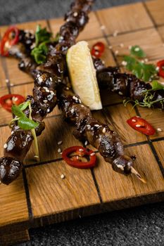 Grilled chicken hearts with lime on wooden skewer, garnished with chili, cilantro, sesame on gray background