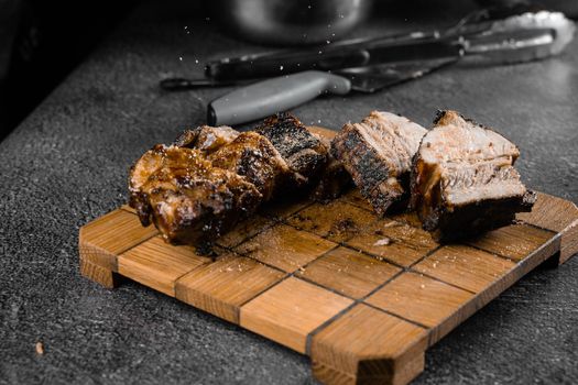 Grilled ribs slicing on a wooden plate on a gray background. Barbecue decoration