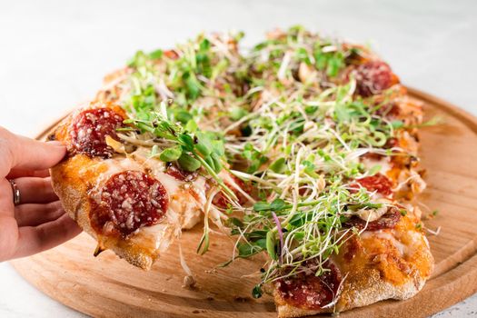 Pinsa romana with salami, cheese, mushrooms, decorated with microgreens on wooden boardon white background