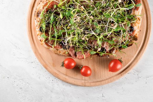 Pinsa romana with salami, cheese, mushrooms, decorated with microgreens on wooden boardon white background