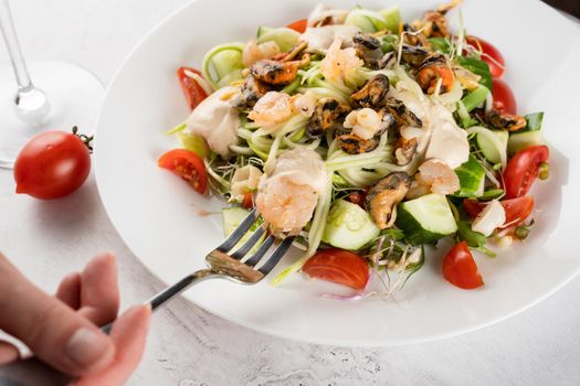 Salad with mussel, shrimp, tomato cherry, cucumber, zucchini pasta, microgreen, yogurt sauce on white plate on light table