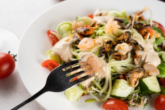 Salad with mussel, shrimp, tomato cherry, cucumber, zucchini pasta, microgreen, yogurt sauce on white plate on light table