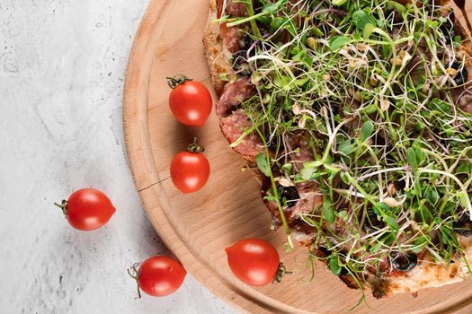 Pinsa romana with salami, cheese, mushrooms, decorated with microgreens on wooden boardon white background