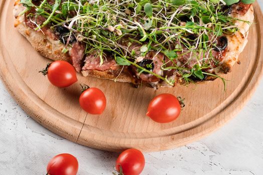 Pinsa romana with salami, cheese, mushrooms, decorated with microgreens on wooden boardon white background