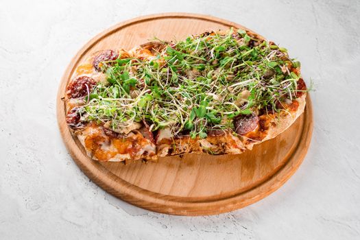 Pinsa romana with salami, cheese, mushrooms, decorated with microgreens on wooden board on white background.