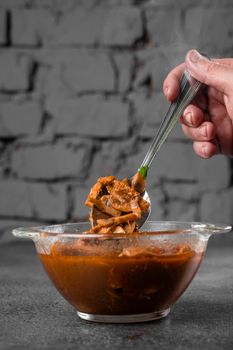 Soup with meat, mushrooms, tomatoes in transparent bowl on gray background. Appetizing thick satisfying tom yam