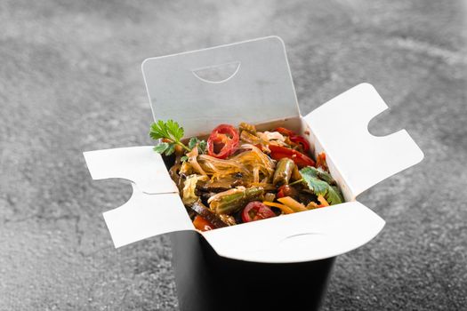 Wok in box rice noodles in black food container. Fast food delivery service. Takeaway chinese street meal